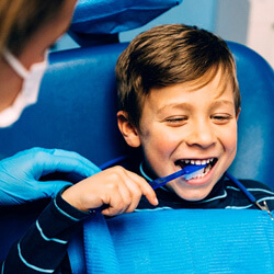 child smiling while brushing his teeth in dental chair