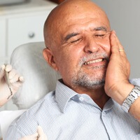 Bald male inneed of root canal therapy painfully touching his cheek