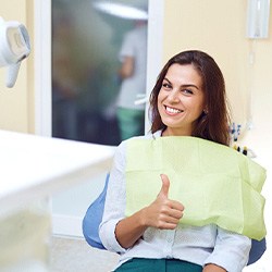 Female patient in a dental chair giving a thumbs-up