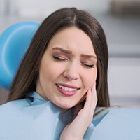 Dark haired woman painfully touching cheek during emergency dentistry visit