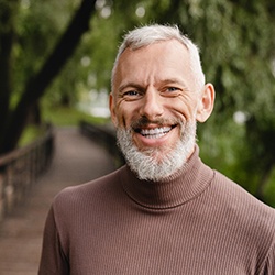 Senior man on bridge smiling with implant dentures in Midwest City, OK