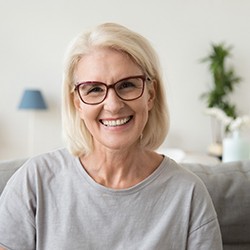 Senior woman with glasses smiling with implant dentures in Midwest City, OK