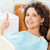 Woman with curly hair holding a thumbs up after oral cancer screening