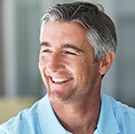 Male wearing a light blue polo smiling after dental implant tooth replacement