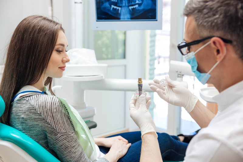 Male dentist showing female patient a dental implant