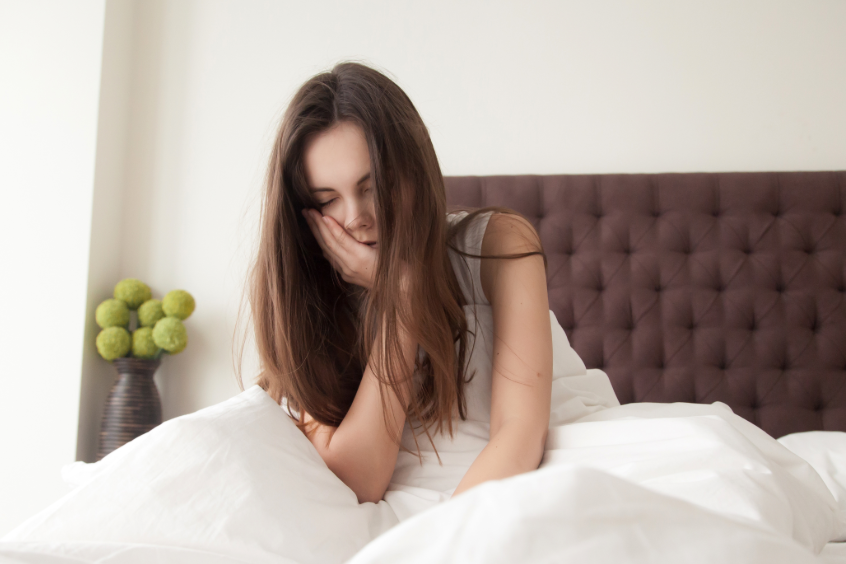 Woman sitting up in bed, holding jaw